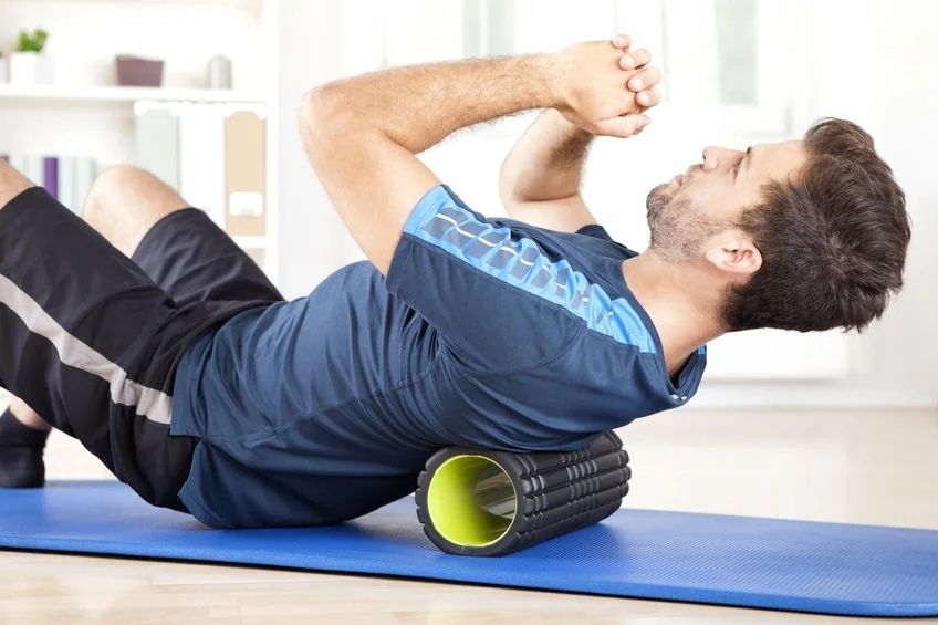 Man rullar ryggen över en foam roller på en träningsmatta